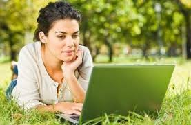 Woman using a computer to Link post blogging just about anywhere as depicted with her laying on her stomach in a field as long as you have internet connectivity!